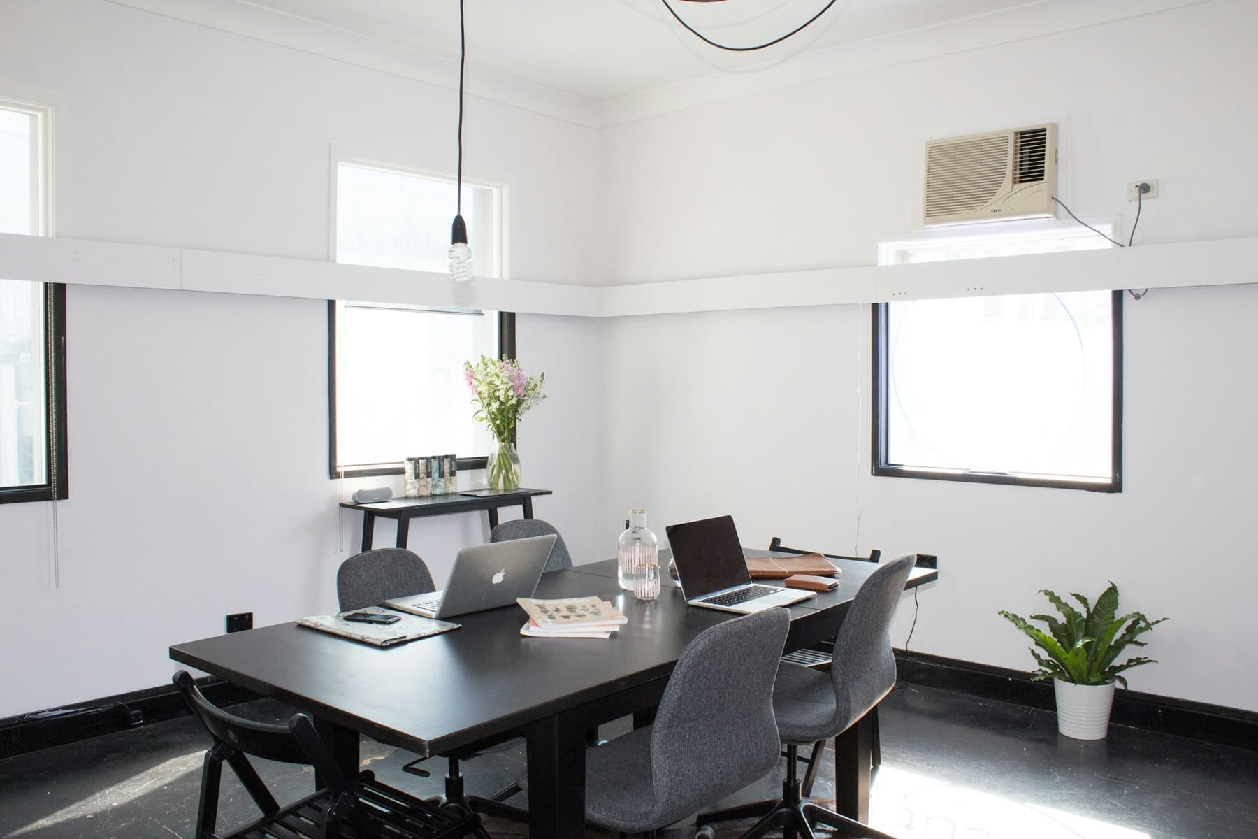 A bright small meeting room with two tall windows and a wooden table with six chairs.